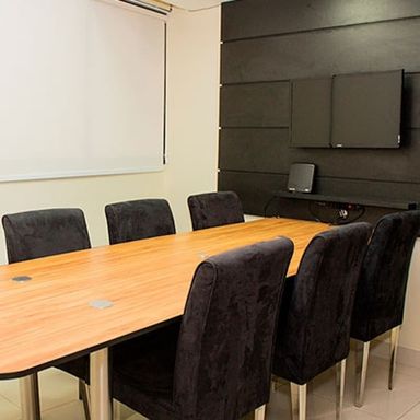 Sala de reunião, com mesa, cadeiras estofadas e televisor.