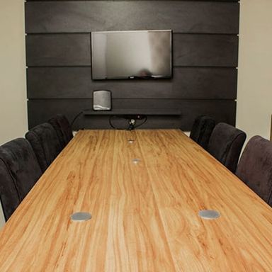 Sala de reunião, com mesa, cadeiras estofadas e televisor.