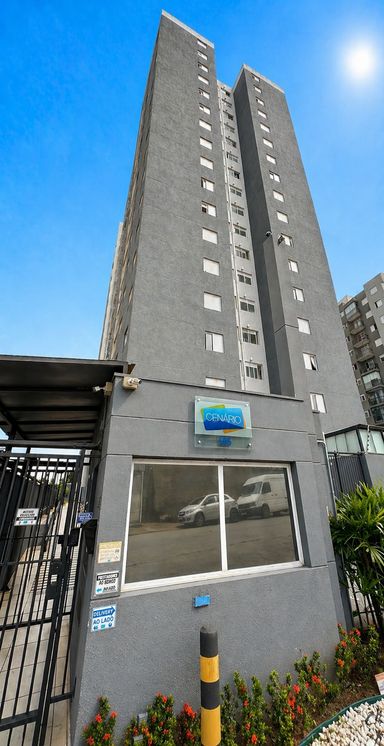 Fachada do Condomínio Cenário, torre residencial com acesso controlado, portaria e entrada organizada, oferecendo praticidade e segurança aos moradores.