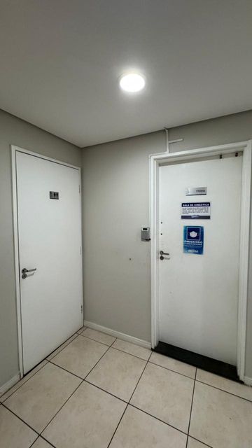 Hall de acesso à sala fitness do condomínio, com controle de entrada e áreas de apoio próximas.