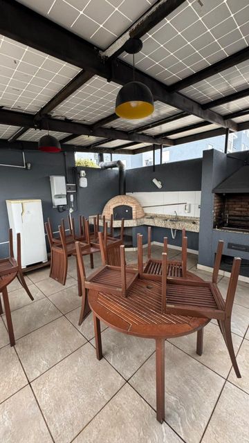 Espaço gourmet externo com churrasqueira, forno de pizza, bancada de apoio, mesas e área coberta, proporcionando um ambiente agradável para receber convidados.
