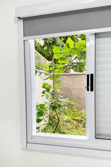 Janela do quarto principal com vista para área verde do apartamento.
