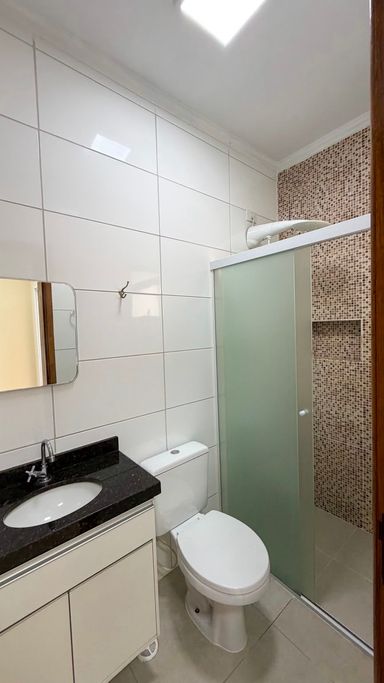 Banheiro social completo, com box de vidro, nicho, revestimento em pastilhas, bancada em granito e gabinete planejado.