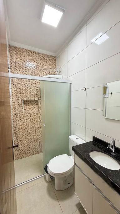 Banheiro completo com box de vidro, nicho embutido, parede em pastilhas, bancada em granito preto e gabinete planejado.