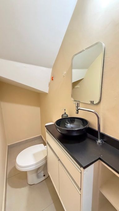 Lavabo com gabinete planejado, bancada em pedra preta, cuba de apoio e ótimo aproveitamento do espaço sob a escada.