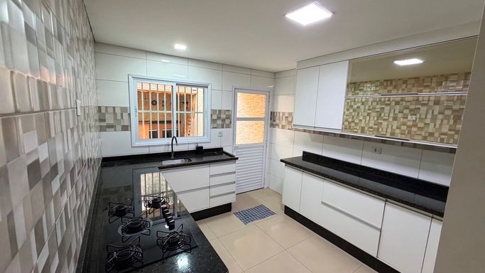 Cozinha planejada e espaçosa, com bancadas em granito preto, cooktop, forno embutido e armários dos dois lados.
