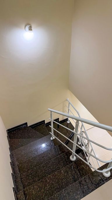 Escada revestida em granito, com corrimãos dos dois lados e caixa de escada com pé-direito elevado.