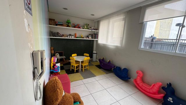 Brinquedoteca com espaço lúdico, brinquedos infantis, mesa de atividades, iluminação natural e ambiente reservado para recreação das crianças.