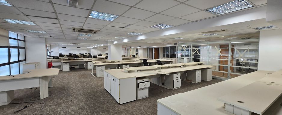 Área de trabalho com bancadas, gaveteiros e divisórias de vidro.