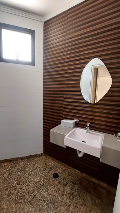 Lavabo charmoso com toque amadeirado e aconchegante. A parede principal tem um painel amadeirado que trás conforto ao ambiente, combina muito be com piso e o espelho moderno.