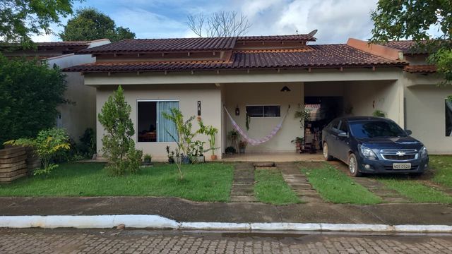 Fachada de residência unifamiliar térrea com cobertura em telhas cerâmicas, recuo frontal gramado com trilhos de concreto para acesso veicular e varanda aberta no Bairro Aeroclube, em Porto Velho-RO.