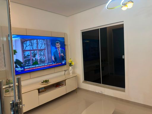 Living social/sala de TV com painel planejado em tons claros, rack suspenso, iluminação decorativa e ampla esquadria de vidro para integração visual no Bairro Aponiã, em Porto Velho-RO.
