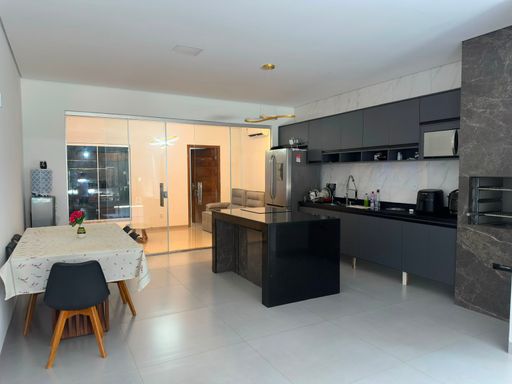 Ampla cozinha gourmet integrada à sala de jantar com piso em porcelanato polido, ilha central e bancadas em granito escuro, além de fechamento em cortina de vidro temperado no Bairro Aponiã, em Porto Velho-RO.
