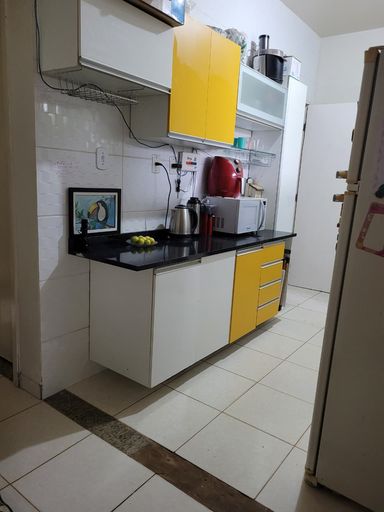 Vista em perspectiva da bancada de granito da cozinha com marcenaria planejada inferior combinando tons de branco e amarelo no Bairro Aeroclube, em Porto Velho-RO.
