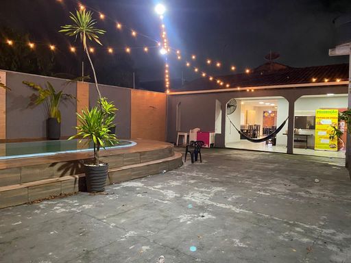 Área de lazer externa com pátio pavimentado em concreto, deck elevado com piscina e iluminação aérea por varal de luzes para eventos noturnos no Bairro Esperança da Comunidade, em Porto Velho-RO.