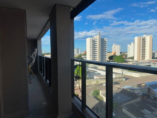 Vista interna do living social em direção à varanda gourmet, destacando o guarda-corpo panorâmico em vidro escuro e perfis metálicos pretos no Bairro Olaria, em Porto Velho-RO.