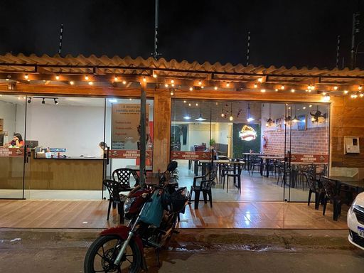 Vista externa frontal do estabelecimento à noite, ressaltando o apelo comercial da iluminação decorativa e o acesso direto ao salão de atendimento no Bairro Esperança da Comunidade, em Porto Velho-RO.