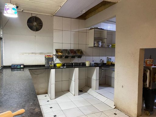 Área técnica de cozinha e preparação com bancadas em granito escuro, revestimento cerâmico nas paredes e piso, além de coifa/exaustor industrial instalado no Bairro Esperança da Comunidade, em Porto Velho-RO.