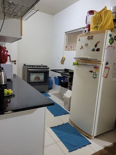 Cozinha em estilo corredor com bancada em granito escuro, armários aéreos compactos e revestimento cerâmico nas paredes de área molhada no Bairro Aeroclube, em Porto Velho-RO.