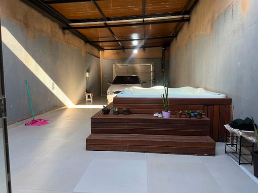 Área de lazer e relaxamento privativa nos fundos, equipada com banheira de hidromassagem/ofurô sobre deck de madeira elevado e cobertura em estrutura metálica aparente no Bairro Aponiã, em Porto Velho-RO.