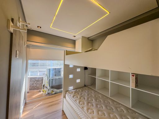 Dormitório com beliche planejado

Quarto infantil com beliche de madeira branca e sancas iluminadas.

Este quarto otimiza o espaço vertical com um beliche planejado em madeira branca, apresentando nichos organizadores integrados na estrutura inferior. O teto de gesso possui uma sanca retangular com iluminação de LED que define a área central do cômodo. Grandes janelas com esquadrias de alumínio oferecem vista para o condomínio, garantindo ventilação constante. A paleta de cores claras e o piso laminado transmitem uma sensação de higiene e amplitude, ideal para uma estética juvenil organizada e termicamente agradável.