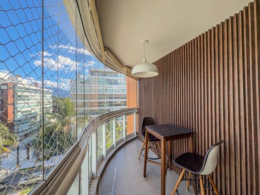 Sacada envidraçada com deck

Varanda curva com fechamento em vidro e mobiliário de madeira.

Esta sacada panorâmica apresenta um design curvilíneo protegido por envidraçamento total. O piso é revestido com deck de madeira natural, proporcionando um toque orgânico e confortável para os pés. Uma mesa alta de madeira com bancos acolchoados em tecido cinza convida à contemplação da vista urbana. A parede lateral em madeira ripada harmoniza com o mobiliário, enquanto a iluminação pendente branca garante charme durante a noite. O ambiente transmite frescor, liberdade e uma estética de resort urbano privativo.