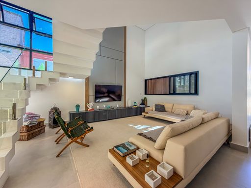 Sala de estar com pé-direito duplo

Sala de estar ampla com pé-direito duplo e sofá branco.

Esta sala de estar sofisticada apresenta um pé-direito duplo impressionante que amplia visualmente o espaço. O ambiente é dominado por tons neutros, com paredes brancas e piso em porcelanato claro. Um grande sofá modular branco está disposto em formato de L sobre um tapete felpudo cinza, acompanhado por duas poltronas de design moderno com estampa geométrica. O mobiliário inclui um rack baixo para a TV e uma estante de nichos com detalhes em espelho. A iluminação natural é abundante, proveniente de uma janela alta e uma porta de correr que se abre para o exterior. A sensação é de amplitude, frescor e conforto contemporâneo.