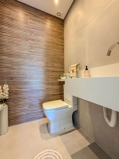 Lavabo com textura de parede

Lavabo com cuba esculpida e parede com textura orgânica.

Este lavabo apresenta um design minimalista com foco nas texturas. A parede ao fundo do vaso sanitário possui um revestimento texturizado em tons de marrom e bege com padrão orgânico ondulado. A bancada é em material sintético branco com cuba esculpida e torneira de parede cromada. O piso é em porcelanato cinza claro, e a iluminação é suave, proveniente de um ponto de luz embutido no teto. O ambiente é compacto e sofisticado, com uma estética limpa e moderna.
