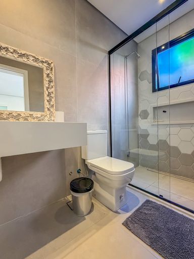 Banheiro com detalhes em pastilha

Banheiro com bancada em mármore e detalhes em pastilhas hexagonais.

Este banheiro apresenta um design clean e funcional, com destaque para a bancada em mármore creme com cuba de sobrepor branca e torneira cromada. O vaso sanitário é branco, e o box é delimitado por portas de vidro temperado transparente com esquadrias escuras. O revestimento das paredes combina azulejos cinza claro com detalhe em pastilhas hexagonais dentro do box. O piso é em porcelanato cinza. A iluminação é suave, com pontos de luz embutidos no teto. O ambiente é limpo e sofisticado, com uma estética contemporânea.