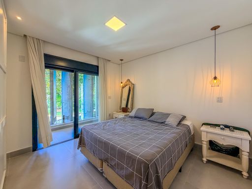 Quarto com cama de casal

Quarto de casal com cama queen e mobiliário em madeira clara.

O quarto de casal exibe um design aconchegante e funcional, com destaque para a cabeceira da cama em madeira clara com ripas horizontais. A cama queen está arrumada com lençóis claros e colcha texturizada. O mobiliário inclui uma cômoda alta em madeira e metal no canto, uma mesa de cabeceira pequena e um criado-mudo. O piso é em laminado de madeira, e as paredes são brancas. A janela com esquadria escura oferece vista para o exterior e possui persiana integrada. A iluminação é suave, com um ponto de luz central no teto. O ambiente transmite tranquilidade e conforto térmico.