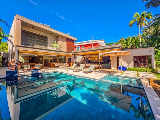 Fachada posterior e piscina

Vista completa da residência a partir da piscina com arquitetura moderna.

A fachada posterior da casa revela uma estrutura de dois pavimentos com grandes painéis de vidro e varandas superiores. O piso térreo abre-se inteiramente para a piscina, eliminando barreiras entre o interior e o exterior. Espreguiçadeiras e mesas de apoio estão dispostas pelo deck de pedra clara, valorizando o espaço ao ar livre. A arquitetura utiliza madeira e vidro para criar uma estética de luxo leve e integrado à natureza, com excelente ventilação natural.