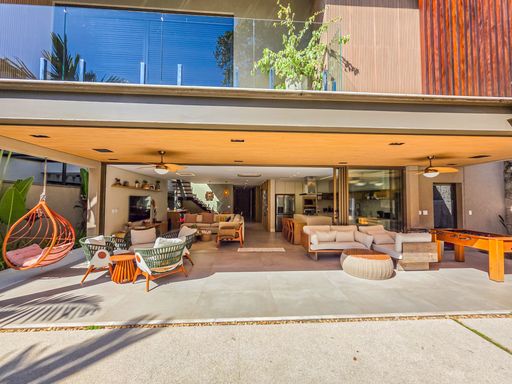 Fachada aberta e terraço

Vista da residência a partir do jardim destacando integração total do térreo.

A arquitetura moderna permite que o living interno e a varanda gourmet se fundam em um único espaço de convivência sem portas aparentes. O mobiliário de design, como as poltronas estampadas e o sofá modular, estão dispostos para o máximo conforto social. No piso superior, as sacadas de vidro e madeira complementam o visual contemporâneo. A estética é de luxo integrado e fluidez espacial, transmitindo uma sensação de amplitude e liberdade térmica inigualável.