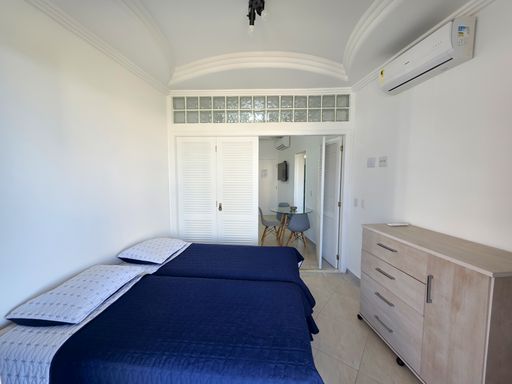 Dormitório de casal climatizado.

Quarto com cama de casal azul e ar-condicionado.

Este quarto principal apresenta uma cama de casal com enxoval em azul marinho, contrastando com o ambiente totalmente branco. O teto trabalhado em gesso inclui luminárias discretas, e o ar-condicionado Split garante a temperatura ideal para o descanso. Ao lado da cama, uma cômoda em madeira clara oferece suporte funcional. A iluminação suave e as paredes claras criam uma estética de serenidade e organização, proporcionando uma sensação térmica de frescor e tranquilidade necessária para o sono.