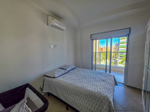 Dormitório com acesso à varanda.

Quarto com cama de casal branca e porta-balcão de vidro.

O segundo dormitório oferece acesso direto à varanda através de uma porta-balcão de alumínio e vidro, permitindo uma excelente circulação de ar e entrada de luz natural. A cama está vestida com colcha branca de padrão geométrico discreto, mantendo a neutralidade do quarto. O piso cerâmico acompanha o padrão do restante do imóvel, facilitando a limpeza. A vista externa integrada ao quarto proporciona uma sensação de liberdade e relaxamento, com uma estética leve e arejada.