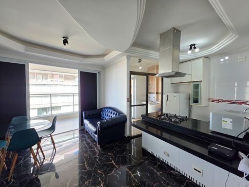 Conceito aberto sala e cozinha.

Visão integrada da sala de jantar e balcão da cozinha americana.

A integração entre os ambientes é o destaque desta imagem, onde o balcão de granito preto separa de forma funcional a cozinha da sala de jantar. O mobiliário segue uma linha moderna, com destaque para as cadeiras coloridas e o sofá de couro. O teto trabalhado em gesso percorre todo o espaço, unificando a estética. Materiais como pedra, couro, vidro e madeira clara nas pernas das cadeiras criam um mix de texturas rico e elegante. O ambiente é amplo, iluminado e visualmente impactante.