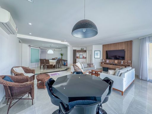 Sala integrada com mesa octogonal
Sala de estar e jantar integrada com mesa preta em primeiro plano.
O amplo living integrado em image_6594fe.jpg conta com uma mesa octogonal preta brilhante com cadeiras escuras sob uma luminária pendente moderna em formato de cúpula. Ao fundo, o espaço se abre para uma sala de TV com painel de madeira e sofás confortáveis, além de uma mesa de jantar de madeira ao fundo. O piso em porcelanato polido claro reflete a iluminação embutida no teto de gesso, criando uma sensação térmica agradável e uma estética altamente sofisticada e fluida.