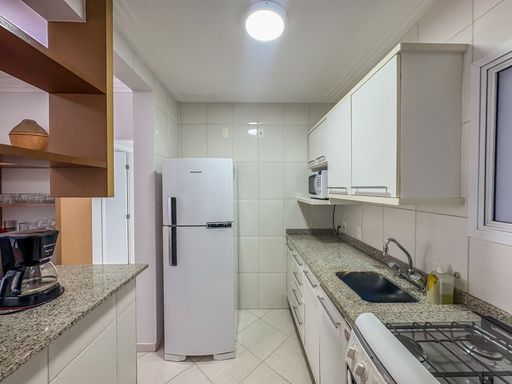 Cozinha planejada clara e moderna

Cozinha estreita com armários brancos, bancada de granito e geladeira duplex.

A cozinha segue o estilo corredor, otimizando cada metro quadrado com armários planejados brancos e puxadores discretos. A bancada em granito sal e pimenta abriga a pia e oferece espaço para preparo, contrastando com o revestimento cerâmico branco das paredes. Eletrodomésticos em branco e inox completam a funcionalidade. A iluminação central em LED garante visibilidade total, resultando em uma estética higiênica, moderna e altamente funcional para o dia a dia.