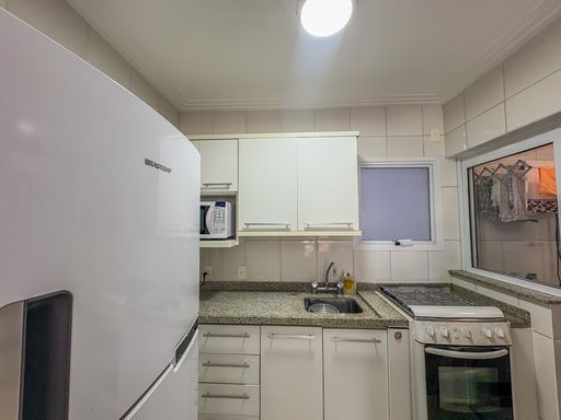 Detalhe funcional da cozinha compacta

Bancada de granito com pia de inox sob armários superiores brancos.

A cozinha é equipada com marcenaria sob medida que aproveita o espaço aéreo para armazenamento. A bancada de granito escuro cria um contraste elegante com os armários brancos foscos. O micro-ondas está embutido em um nicho planejado, liberando espaço de bancada. O piso cerâmico claro com detalhes pretos confere personalidade ao ambiente. A estética é de uma cozinha urbana eficiente, onde a praticidade é a prioridade sem abdicar do design clean.