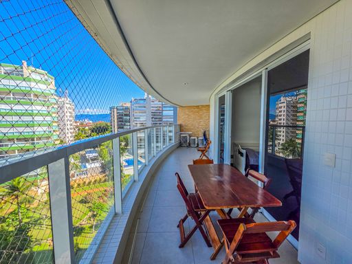 Varanda gourmet para refeições.

Mesa de madeira em varanda com vista para jardim interno.

Esta perspectiva da varanda destaca o conjunto de jantar em madeira maciça, posicionado estrategicamente para aproveitar a vista do paisagismo interno do condomínio. A rede de proteção e o guarda-corpo de vidro garantem a segurança dos moradores. O teto possui acabamento em gesso com iluminação embutida, permitindo o uso do espaço durante a noite. A estética é equilibrada e funcional, proporcionando um refúgio térmico agradável para momentos de relaxamento em família, cercado por tons de verde e o azul do céu.