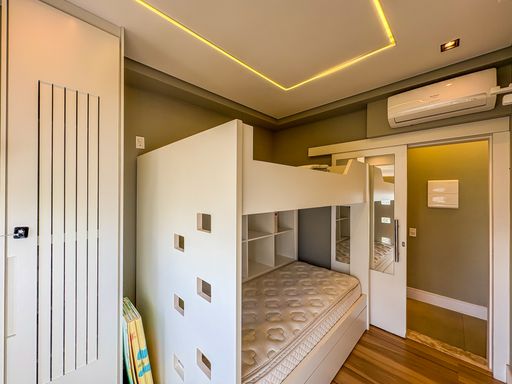 Quarto juvenil otimizado

Beliche moderno com escada de nichos e iluminação embutida.

A marcenaria inteligente deste dormitório inclui um beliche com guarda-corpo de design geométrico e uma escada que funciona como estante de nichos. O teto rebaixado com iluminação de LED cria um efeito cênico acolhedor, enquanto o ar-condicionado split garante a climatização. A porta de correr espelhada otimiza o espaço de circulação e reflete a claridade natural da janela. Materiais como MDF branco, metal e madeira laminada compõem uma estética contemporânea, prática e funcional para o cotidiano.