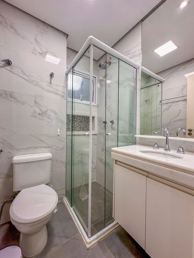 Banheiro moderno com box de mármore

Banheiro social com bancada branca, espelho grande e box com revestimento cinza.

Um banheiro social limpo e minimalista com acabamentos de primeira linha. Conta com uma bancada suspensa de quartzo branco com cuba embutida e metais sanitários cromados de design quadrado. O box de vidro temperado transparente destaca o revestimento interno das paredes em porcelanato que imita mármore ou pedra natural cinza com veios suaves. Um amplo espelho cobrindo a parede superior amplia o espaço compacto, garantindo uma iluminação uniforme, sensação de higiene absoluta e frescor estético.