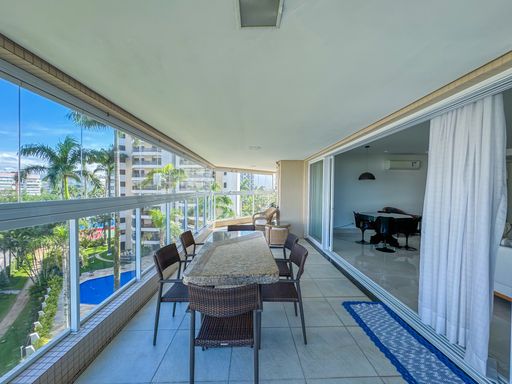 Varanda integrada com mesa comprida
Varanda comprida com mesa de jantar, fechamento de vidro e vista para a piscina.
Perspectiva oposta da varanda gourmet mostrando a extensão do ambiente com fechamento em vidro retrátil. Uma longa mesa de refeições com tampo de granito e cadeiras tramadas organiza o espaço, complementada por um tapete passadeira azul que direciona o fluxo em direção às portas de correr que dão acesso à sala de estar climatizada. O ambiente exibe uma decoração clean, com teto rebaixado em gesso e iluminação embutida discreta, evocando conforto térmico e elegância.Mesa de jantar na varanda
Mesa de jantar gourmet com cadeiras na varanda e prédios ao fundo.
Ambiente de refeições ao ar livre posicionado estrategicamente na varanda envidraçada. A mesa retangular com tampo robusto de pedra natural acomoda confortavelmente seis cadeiras de design ergonômico em fibra sintética escura. O piso cerâmico de tons neutros reflete a claridade natural do dia, enquanto a vista de fundo revela a arquitetura urbana litorânea mesclada com a paisagem natural, gerando uma atmosfera sofisticada e ideal para recepções familiares.Mesa de jantar na varanda
Mesa de jantar gourmet com cadeiras na varanda e prédios ao fundo.
Ambiente de refeições ao ar livre posicionado estrategicamente na varanda envidraçada. A mesa retangular com tampo robusto de pedra natural acomoda confortavelmente seis cadeiras de design ergonômico em fibra sintética escura. O piso cerâmico de tons neutros reflete a claridade natural do dia, enquanto a vista de fundo revela a arquitetura urbana litorânea mesclada com a paisagem natural, gerando uma atmosfera sofisticada e ideal para recepções familiares.