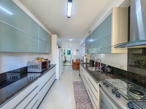 Cozinha planejada estilo corredor
Cozinha comprida com armários aéreos cinza-azulados e bancadas de granito escuro.
Esta cozinha planejada em formato de corredor otimiza o espaço com bancadas de granito preto em ambos os lados e armários planejados inferiores e superiores com portas em tom cinza-azulado reflexivo. Do lado direito, um fogão embutido de inox com coifa se destaca, enquanto eletrodomésticos como forno e micro-ondas ocupam a bancada oposta. A iluminação central em calha de LED garante ótima visibilidade, reforçando a sensação térmica limpa e organizada.