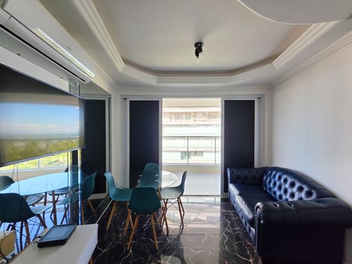 Sala de estar moderna integrada.

Interior de sala com sofá de couro preto e mesa de jantar.

Uma sala de estar sofisticada com teto de gesso rebaixado e iluminação embutida em sancas fluidas. O ambiente conta com um sofá de couro capitonê em tom azul-marinho e uma mesa de jantar redonda com tampo de vidro e cadeiras modernas em turquesa. O piso de porcelanato preto com veios brancos (estilo marmorizado) confere um brilho luxuoso e uma estética contemporânea. A climatização por ar-condicionado Split garante o conforto térmico, enquanto as janelas amplas trazem a claridade externa para o interior.