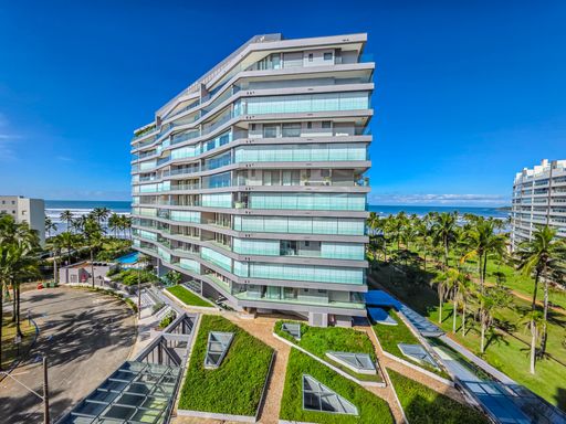 Edifício moderno à beira-mar da Riviera.

Fachada de prédio residencial de luxo com arquitetura contemporânea e jardins.

A imagem destaca a fachada imponente de um edifício residencial de alto padrão, caracterizado por linhas arquitetônicas horizontais e amplas varandas envidraçadas. O entorno é composto por um projeto de paisagismo sofisticado que inclui gramados impecáveis e áreas de circulação com design geométrico. A iluminação solar direta ressalta os tons de cinza e branco da estrutura, enquanto o céu azul e a proximidade com coqueiros reforçam a estética litorânea. É um ambiente que transmite modernidade e exclusividade
