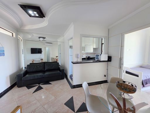 Cozinha americana e sala jantar.

Ambiente integrado com balcão de granito preto e mesa de vidro.

A imagem exibe o conceito aberto do imóvel, onde a cozinha é separada da área social por um balcão funcional em granito preto. A sala de jantar conta com uma mesa redonda de vidro e cadeiras de design moderno, otimizando o espaço. O uso de materiais como pedra, vidro e couro cria uma estética urbana e elegante. A iluminação é composta por pontos de luz embutidos e claridade natural. A disposição dos móveis favorece a circulação, transmitindo uma sensação de organização, frescor e modernidade.