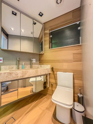 Banheiro clean com mármore

Banheiro com bancada de mármore crema e cuba de sobrepor de inox.

Este banheiro social exibe uma estética limpa e sofisticada com bancada em mármore de tom bege claro. A cuba esculpida em inox escovado é acompanhada por metais de design minimalista. A parede lateral é revestida com painéis de madeira tratada, conferindo um toque orgânico e aquecendo a sensação térmica do ambiente. O espelho amplo acima da pia reflete a iluminação embutida, enquanto o vaso sanitário de linhas quadradas reforça o design moderno. O uso de pedra natural e madeira cria um contraste elegante e duradouro.