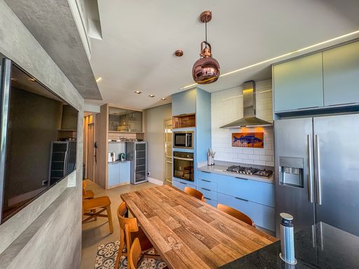 Área gourmet completa

Cozinha equipada com eletrodomésticos inox, mesa rústica e armários cinzas.

A cozinha gourmet é totalmente equipada, apresentando fornos embutidos em torre quente e armários planejados que aproveitam cada espaço. A mesa de madeira maciça serve como centro das atenções, conectando a área de preparo ao convívio. A iluminação trilha o caminho do teto com sancas de LED de alto brilho. O uso de granito escuro nas bancadas e azulejos brancos tipo "subway tile" cria uma estética atemporal e moderna. O ambiente transmite uma sensação de amplitude e eficiência gastronômica de alto nível.