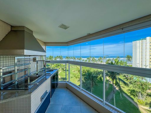 Área da churrasqueira na varanda
Churrasqueira gourmet integrada na bancada de granito da varanda com vista externa.
Espaço gourmet funcional integrado à varanda de frente para o mar, equipado com uma churrasqueira moderna com acabamento em inox e coifa sobreposta. A bancada de trabalho é revestida em granito escuro com pia embutida e armários inferiores planejados em tom cinza. O revestimento da parede em pastilhas claras harmoniza perfeitamente com a iluminação natural abundante proveniente da fachada envidraçada, transmitindo uma estética contemporânea, limpa e convidativa.
