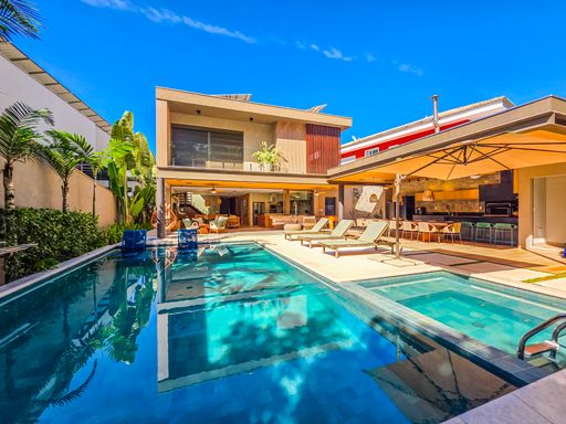 Área de lazer com piscina

Vista externa de residência moderna com piscina iluminada e jardim lateral.  

Uma luxuosa área externa destaca uma piscina retangular com revestimento em tom azul profundo, cercada por um deck de pedra clara e gramado bem cuidado. A arquitetura da casa apresenta linhas retas, com amplas aberturas de vidro e detalhes em madeira que aquecem a estética contemporânea. Espreguiçadeiras confortáveis e um ombrelone de grande porte estão estrategicamente posicionados para o lazer sob o sol. A iluminação externa e o céu azul límpido reforçam uma sensação térmica de frescor e uma estética de resort privado.